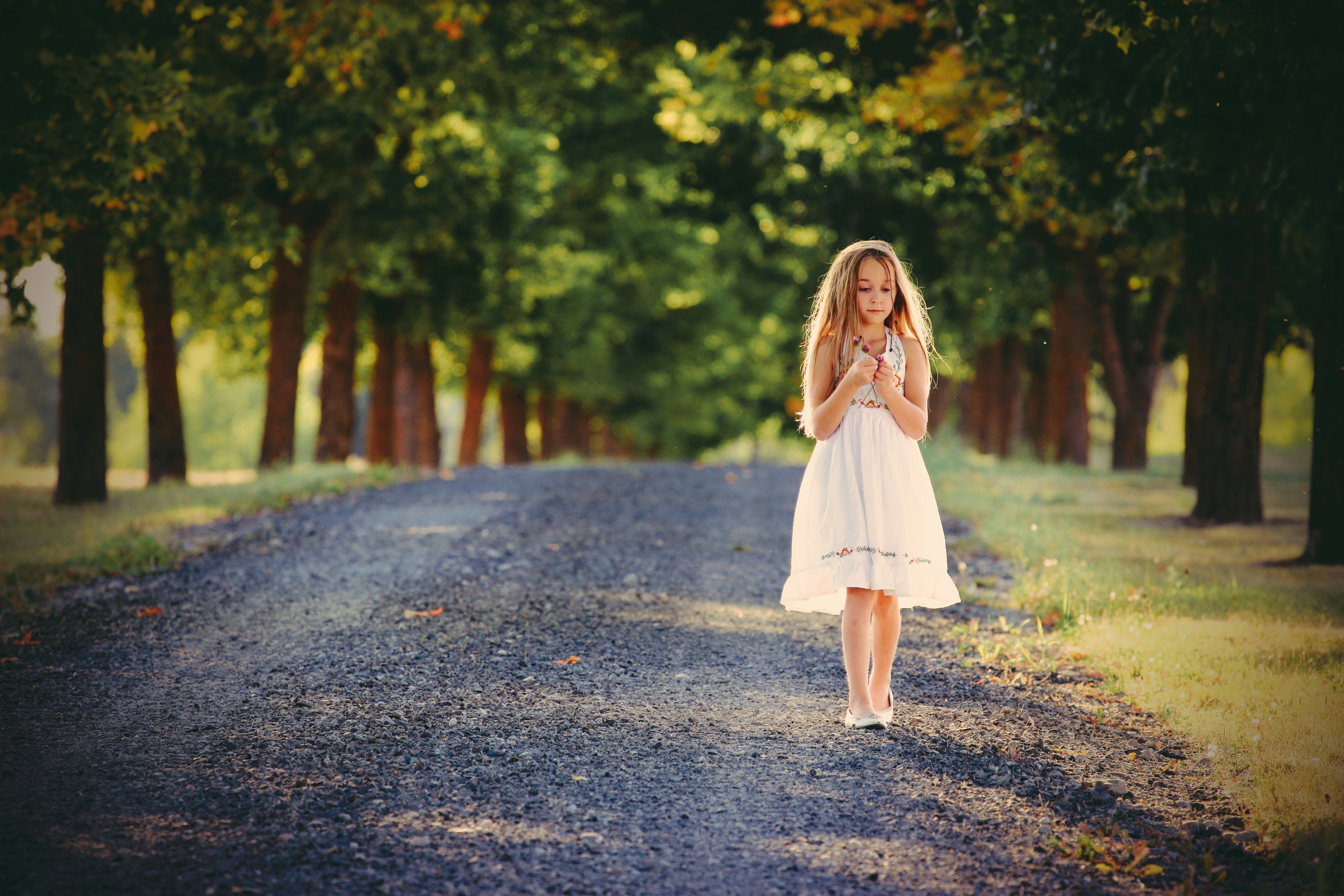 girl standing between green leafed trees